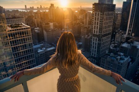 Rich woman enjoy the sunset standing on the balcony at luxury apartments in New York City. Luxury life concept. Succesful B businesswoman relax.