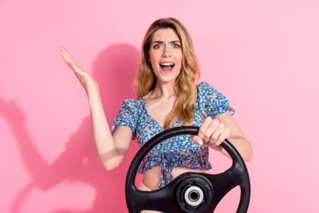 Photo portrait of pretty young girl hold steering wheel annoyed wear trendy blue flower print outfit isolated on pink color background.