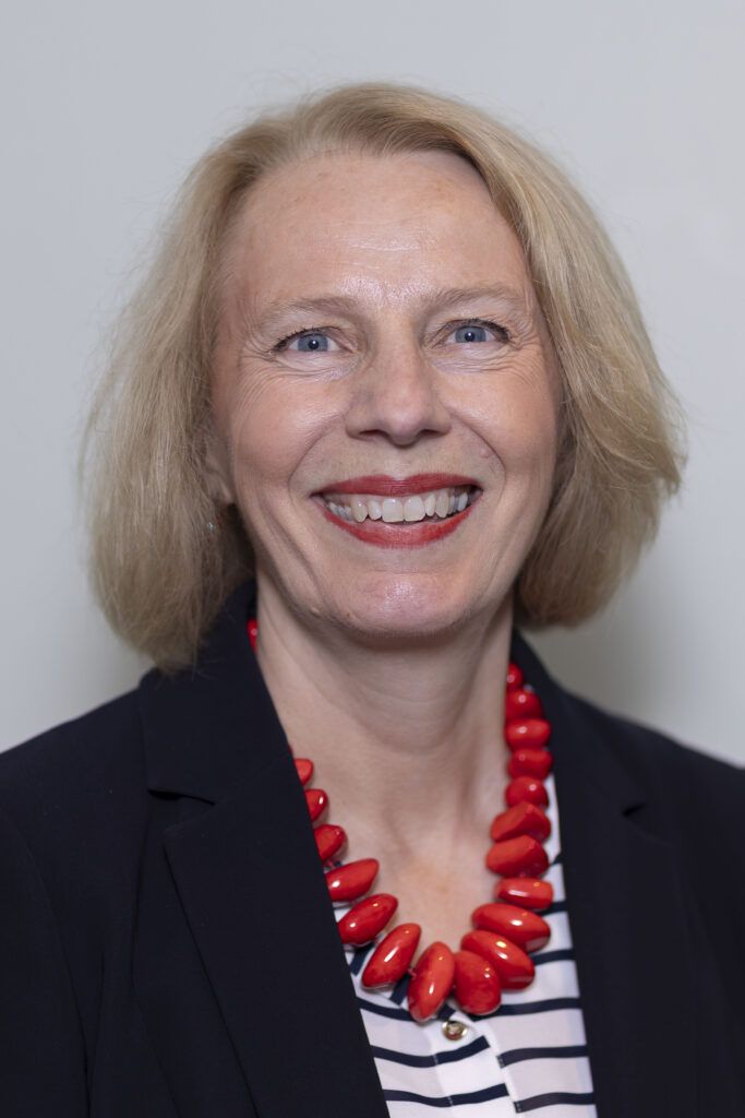 Portrait of middle aged lady with blond hair, blue jacket and orange bead neacklace