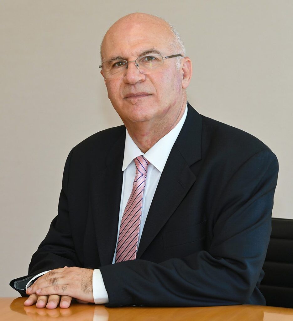 Bald white man sitting in chair in suit and tie with plain background