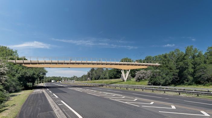 A wood-coloured footbridge over an empty road on a sunny day