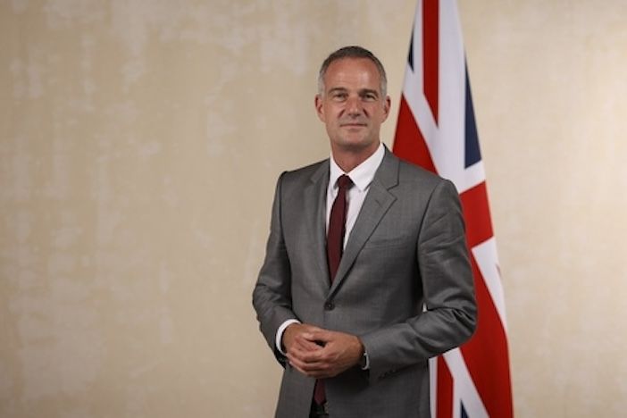 Man in suit stands in front of Union Jack Flag