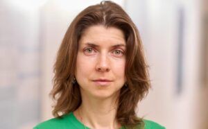 The image shows a woman with shoulder-length brown hair wearing a green top.