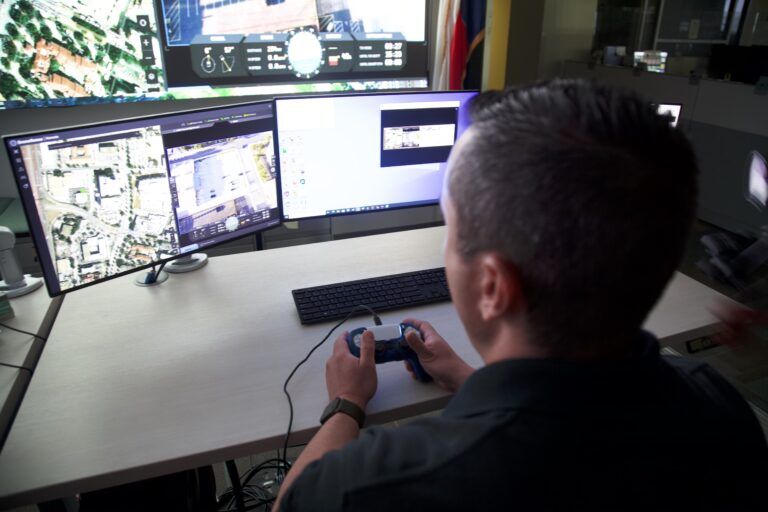 A person sits at a desk with three computer monitors displaying surveillance