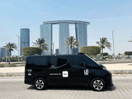 WeRide autonomous vehicle driving on a road in Al Maryah Island's Central Business District, surrounded by modern high-rise buildings and palm trees