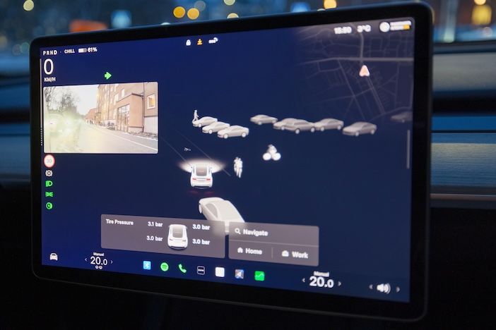 Close up view of Tesla car touchscreen with navigation map rear camera street view traffic visualization and tire pressure data.