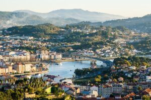 Open view of the south side of the historical city of Pontevedra from an elevated viewpoint. Highway bridge crossing Lerez river. Mountains in background. Sunset.