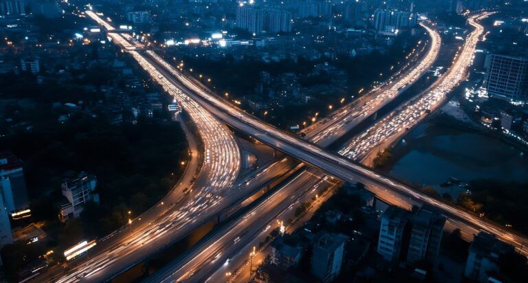 Aerial view of a busy city highway at night with flowing traffic lights and urban skyline