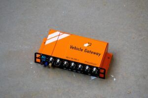 Orange Vehicle Gateway unit by Pilotfish displayed on concrete surface, showing multiple connection ports on the front panel
