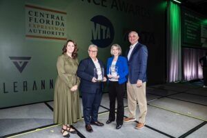Three woman and a man in business attire. Two women in the center hold awards
