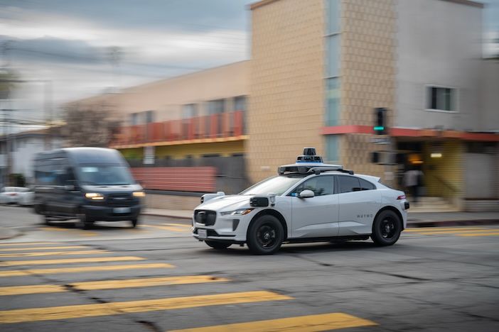 LOS ANGELES, CA - March 11, 2025: Google's Alphabet Waymo driverless self driving taxi cab rushing through city traffic, crossing illuminated street intersection at dusk in West Hollywood, California.