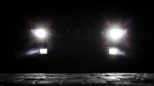 Bright headlights of a vintage car cutting through the darkness at night. Beams and lens flares on the asphalt. Stylized night shot.
