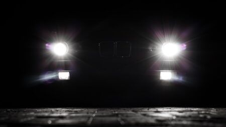 Bright headlights of a vintage car cutting through the darkness at night. Beams and lens flares on the asphalt. Stylized night shot.