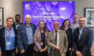 Group of business professionals standing in front of a screen with the words OPEN DAY 33rd ITS WORLD CONGRESS displayed