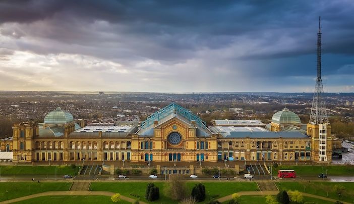 Aerial panromaic view of Alexandra Palace in Alexandra Park with iconic red double-decker bus and dramatic clouds behind