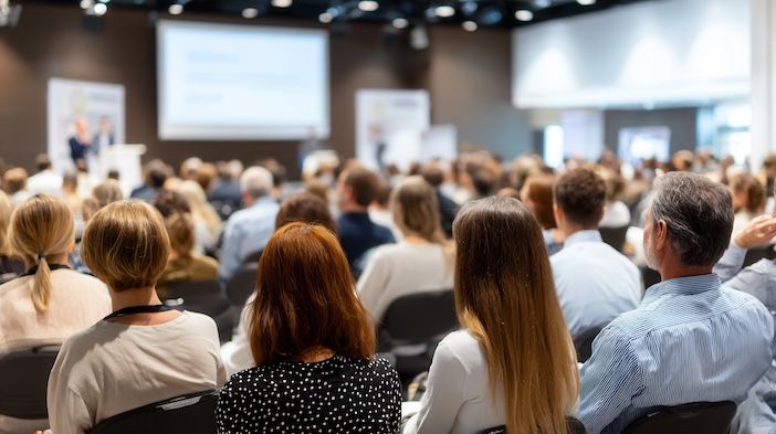 Attendees engaging with a speaker during a dynamic business conference, absorbing insights in a bustling auditorium filled with professionals