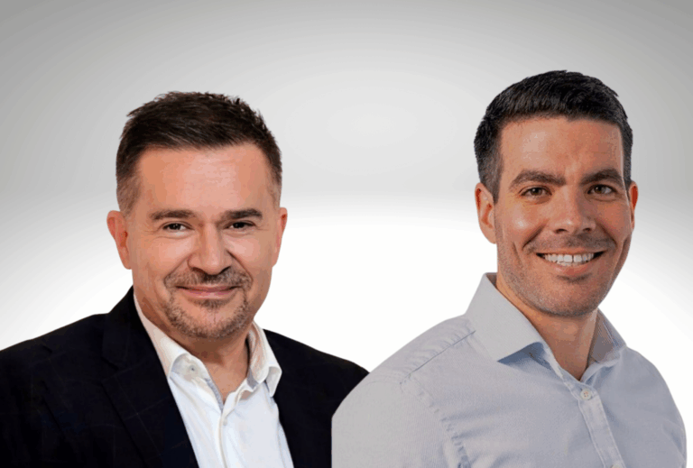 Two white businessmen with short dark hair and clean shaven, both wearing open neck shirts, left one has a jacket