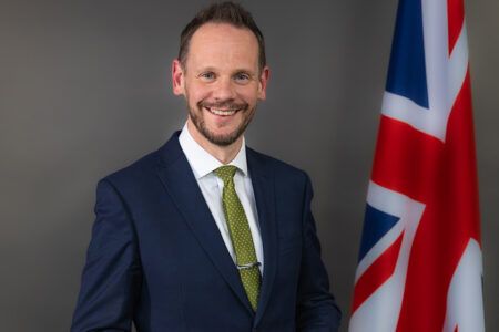 UK launches consultation on automated vehicle regulatory framework Young man white man with short brown beard and short brown hair in suit and tie standing in front of the union jack