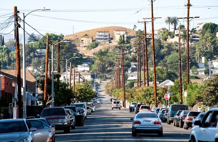Cars parked on a suburban street with hills and palm trees in the background
