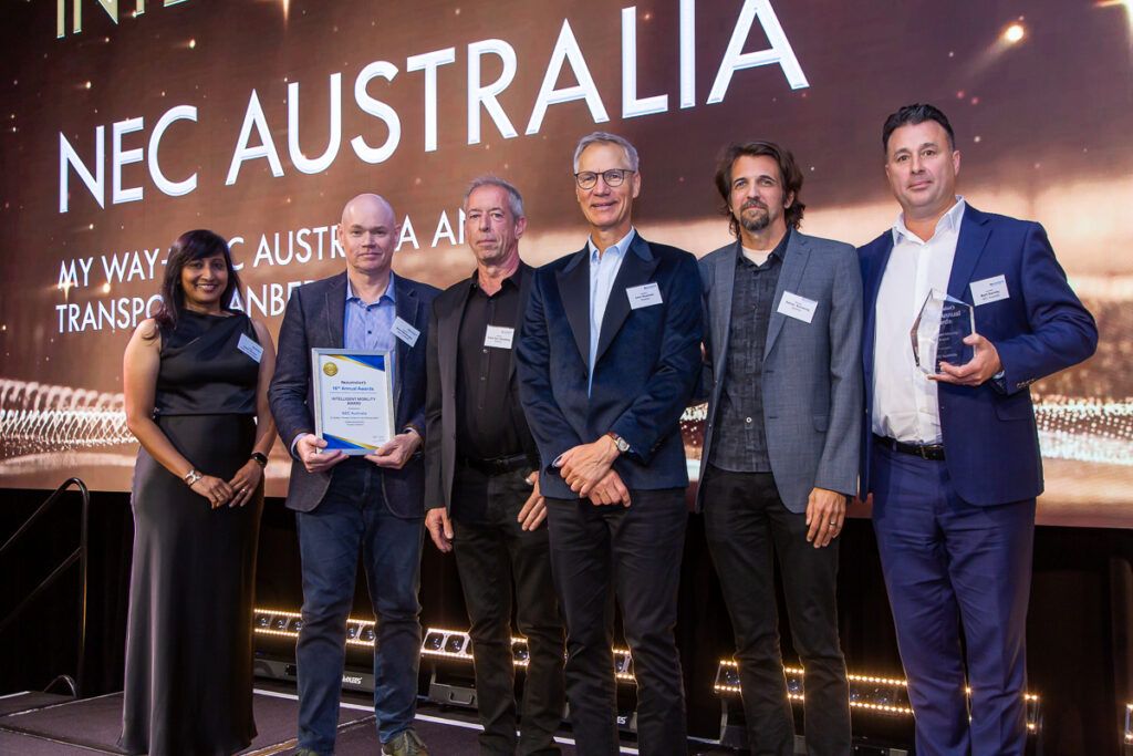 Six people standing on stage at the ITS Australia Awards, with one holding a framed certificate and another holding a glass trophy.