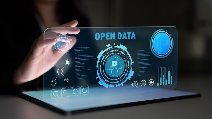 A person interacts with a glowing holographic display showing an open data interface, including an unlocked padlock icon, data visualisation charts, and the words "Open Data", set against a dark background.