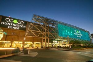 Huntington Place convention centre in Detroit, Michigan, photographed at dusk, with illuminated green and teal signage visible on the building's glass and steel facade.