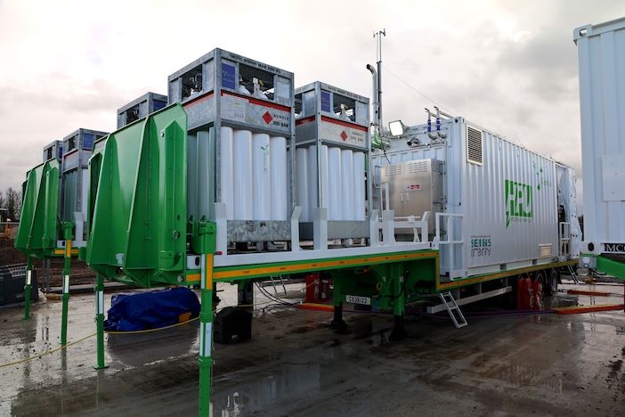 A GeoPura Hydrogen Power Unit mounted on a trailer with green-framed gas storage cylinders, photographed on a wet construction site under an overcast sky.