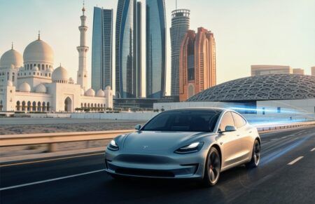 Tesla Full Self-Driving trials get under way on Abu Dhabi roads A silver Tesla saloon car travels along an Abu Dhabi road with digital blue light trails, with the Sheikh Zayed Grand Mosque, Etihad Towers and the Louvre Abu Dhabi visible in the background at dusk