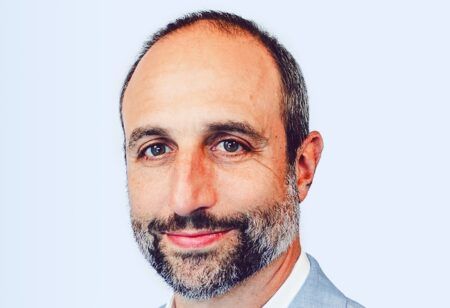 ACES Mobility Coalition names Joshua Schank as executive director Headshot portrait of Joshua Schank, a middle-aged man with a short beard and receding dark hair, wearing a light blue blazer and white open-collar shirt against a pale blue-grey background.