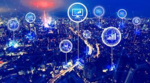 Aerial night view of a city with digital connectivity icons overlaid, representing smart city data networks and intelligent transportation infrastructure.