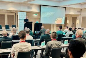 A speaker presents to a seated audience at the ITS Australia Roads, Tolling & Tech 2026 conference, with an Acknowledgement of Country slide visible on the screen behind her