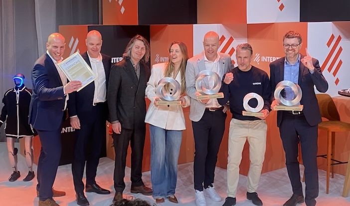 Seven people stand in a line on a stage at Intertraffic Amsterdam, several holding circular silver trophy awards and one holding a certificate, in front of an orange and white branded backdrop.