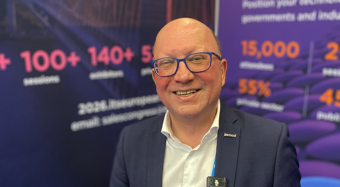 Joost Vantomme, chief executive of ERTICO – ITS Europe, smiling in front of a branded ERTICO display board showing event statistics including 100+ sessions, 140+ exhibitors, and 15,000 attendees.