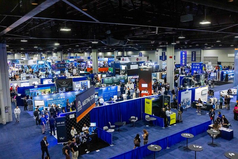 Aerial view of a large indoor exhibition hall filled with technology company stands and attendees at an ITS industry conference