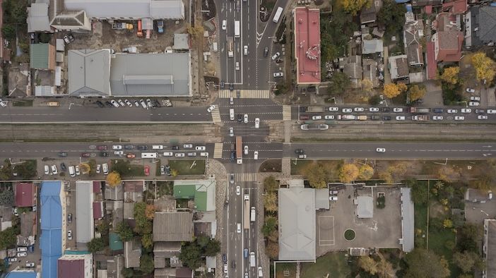  Top-down aerial view of a suburban crossroads showing queued traffic on one approach and free-flowing vehicles on the intersecting road.