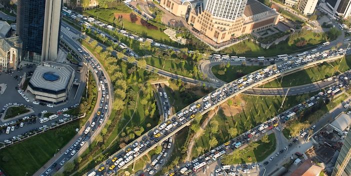 Aerial view of a busy multi-level highway interchange in Istanbul, with heavy traffic visible on all elevated and ground-level carriageways, surrounded by green parkland and high-rise buildings