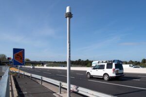 Close-up of a Navtech 360-degree radar unit mounted on a floating-plate bracket atop a roadside pole against a clear blue sky
