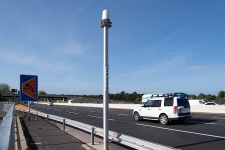 Close-up of a Navtech 360-degree radar unit mounted on a floating-plate bracket atop a roadside pole against a clear blue sky