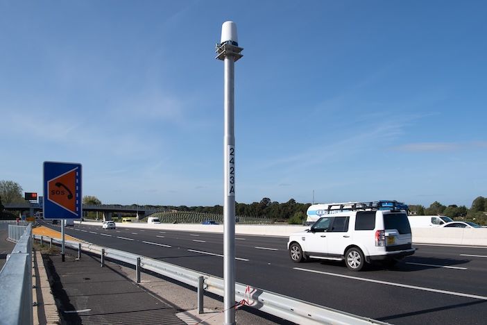 Close-up of a Navtech 360-degree radar unit mounted on a floating-plate bracket atop a roadside pole against a clear blue sky