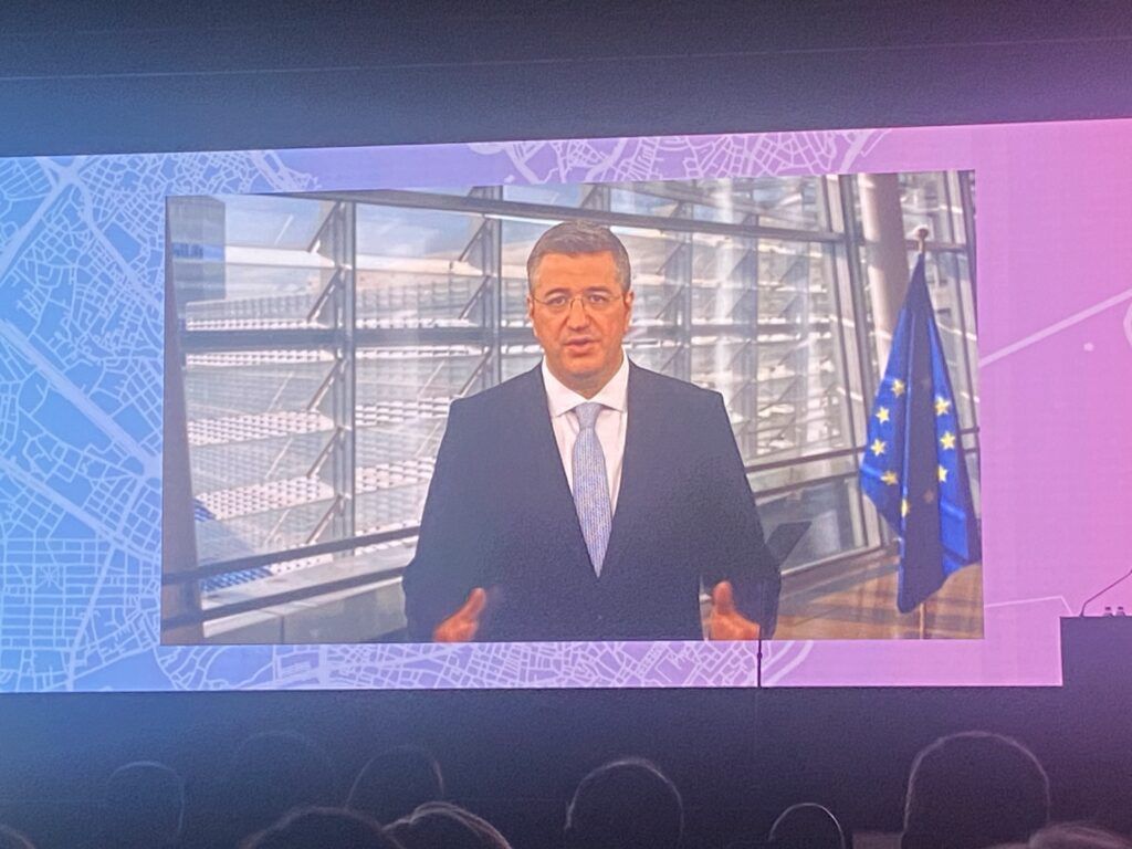 Man in suit with EU flag in the background on a screen in an auditorium