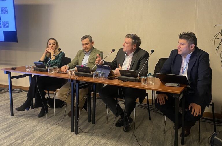 A woman and three men sitting behind a table presenting in a conference session