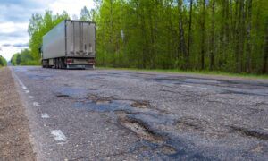 A truck on a rural road which is showing signs of damage