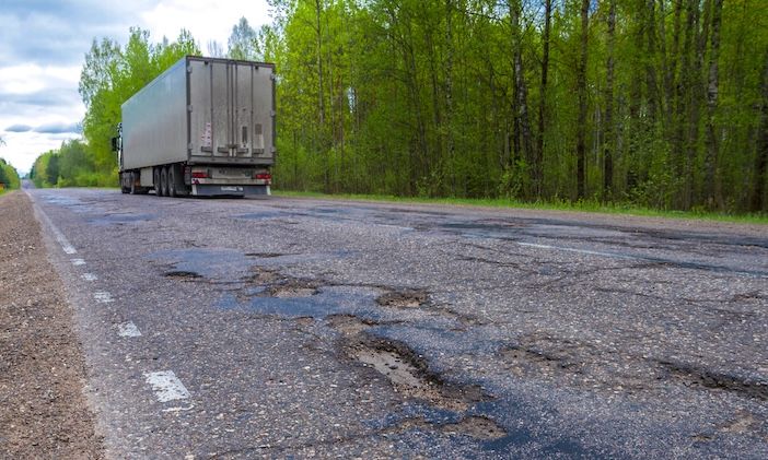 A truck on a rural road which is showing signs of damage