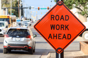Road work ahead warning sign with traffic on city street