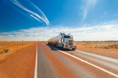 ITS Australia summit to tackle road charging, freight : A tanker truck drives along a straight outback highway in Australia under a clear blue sky, flanked by red desert terrain