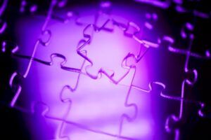 Close-up view of jigsaw puzzle pieces interlocked together, highlighted by purple lighting, emphasizing the shapes and textures of the puzzle