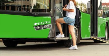 A passenger boarding a green electric bus marked "ELECTRIC" through its front doors, using a boarding ramp