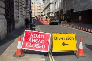 Road Ahead Closed" and "Diversion" signs on a City of London street, with contractors working in the background