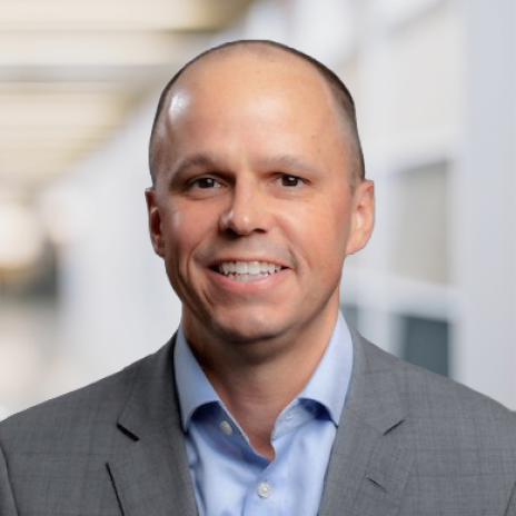 Headshot portrait of Zachary Radford, vice president of policy and government affairs at IBTTA, smiling in a grey blazer and blue shirt