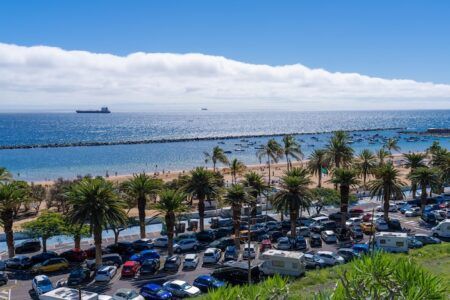 Kapsch TrafficCom launches smart parking project in Tenerife A busy beachfront car park in Santa Cruz de Tenerife lined with palm trees, with the sea and cargo ships visible in the background.